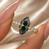Green marquise center stone engagement ring held in fingers